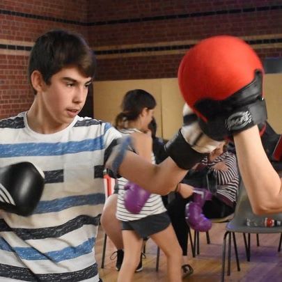 Teen boy with boxing gloves punching a boxing pad.
