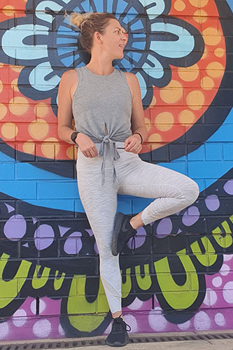 Our trainer Cass standing in front of a coloured wall doing a yoga tree pose.